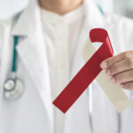 closeup of a dentist in white holding a red and cream ribbon to symbolize oral cancer awareness