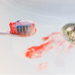 Toothbrush with blood on the bristles over a sink with blood from gum disease