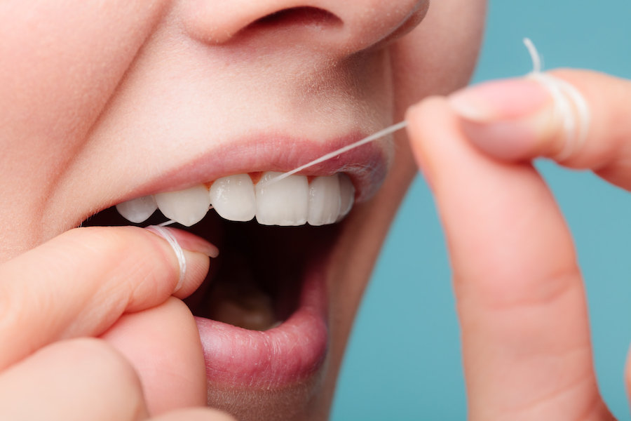 Closeup of a woman flossing between her teeth with string floss against a blue background