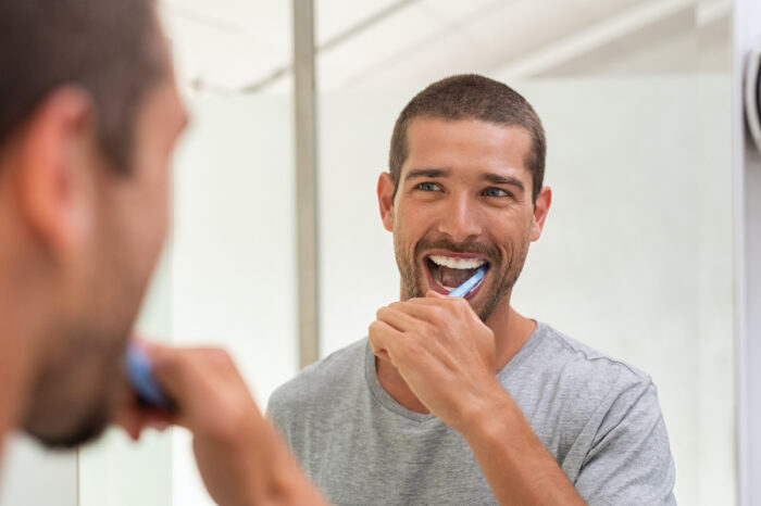 Brunette man smiles at himself in the mirror as he brushes his teeth