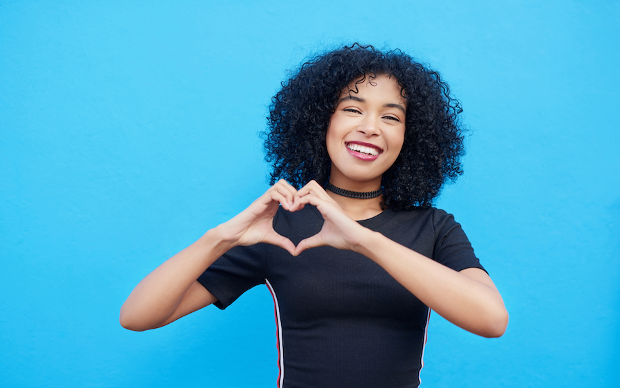 oral health and overall wellness are linked, young Black girl in front of blue background holding hands in a heart shape
