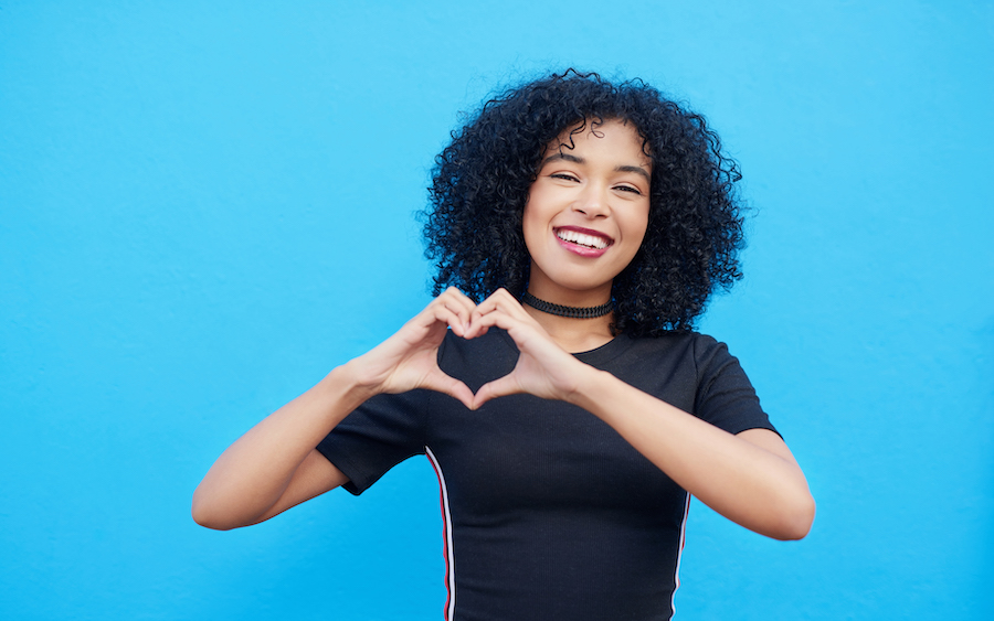 oral health and overall wellness are linked, young Black girl in front of blue background holding hands in a heart shape, dentist in Hot Springs Village